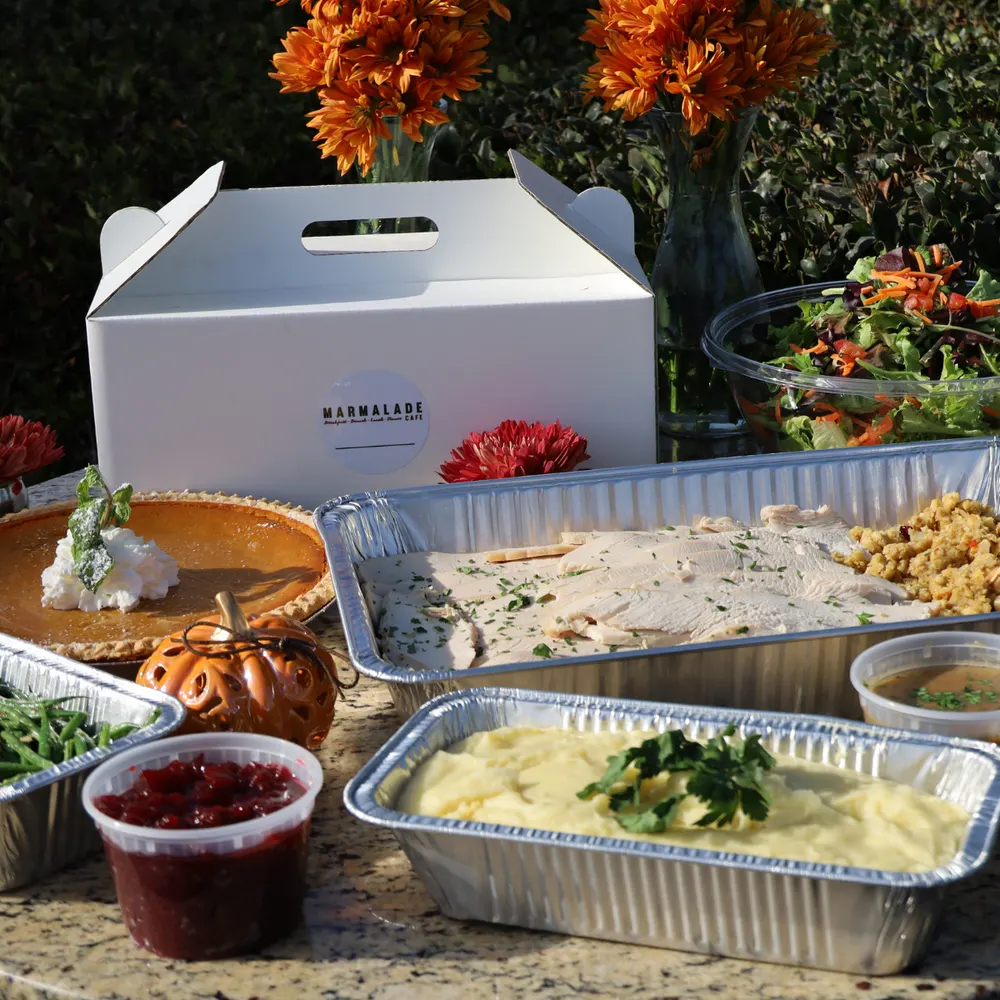 Marmalade Thanksgiving to-go spread with sliced turkey, stuffing, mashed potatoes, green beans, cranberry sauce, salad, and pumpkin pie